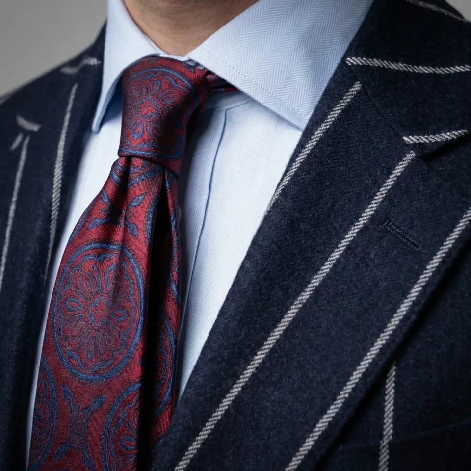 Man wearing a blue pinstripe suit with a red patterned tie and light blue shirt.