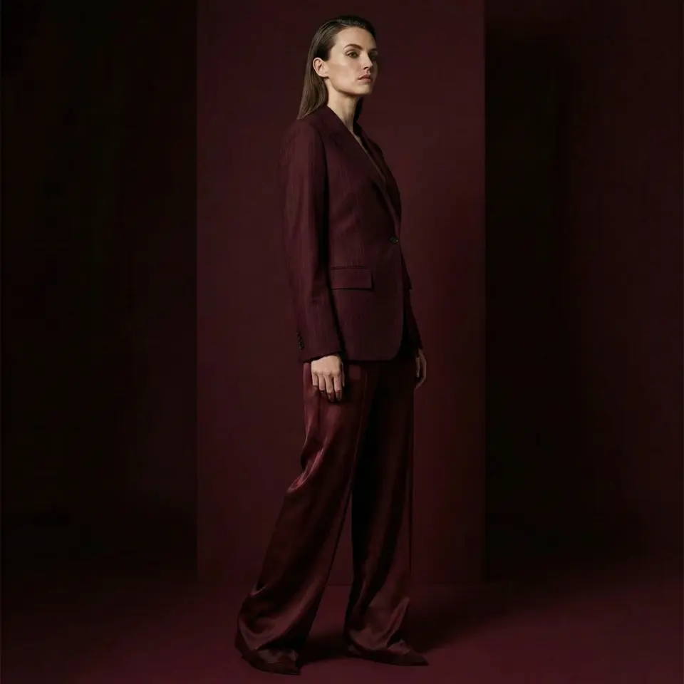 Woman in burgundy suit standing against dark background, showcasing elegant fashion style.
