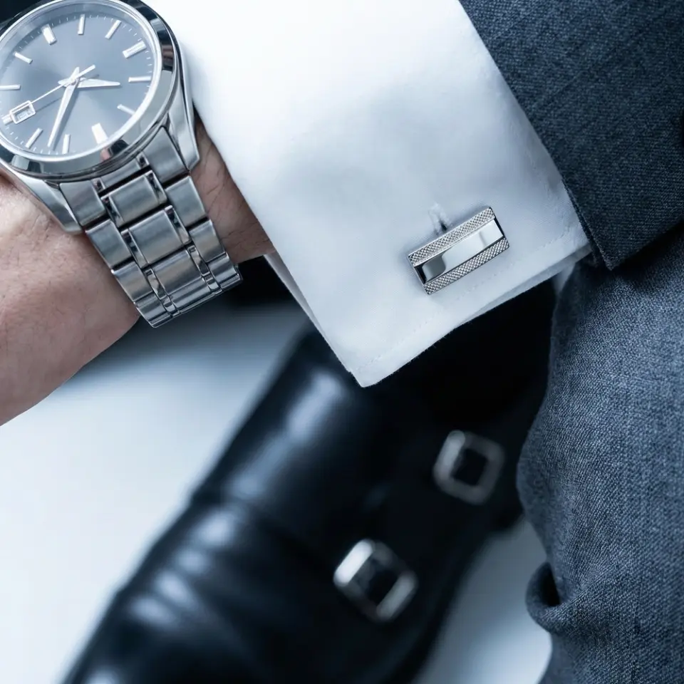 Elegant men's watch with stainless steel band, white shirt cuff, silver cufflinks, and formal black shoes.