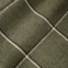Close-up of a green plaid fabric with white and dark stripes creating a crosshatch pattern.