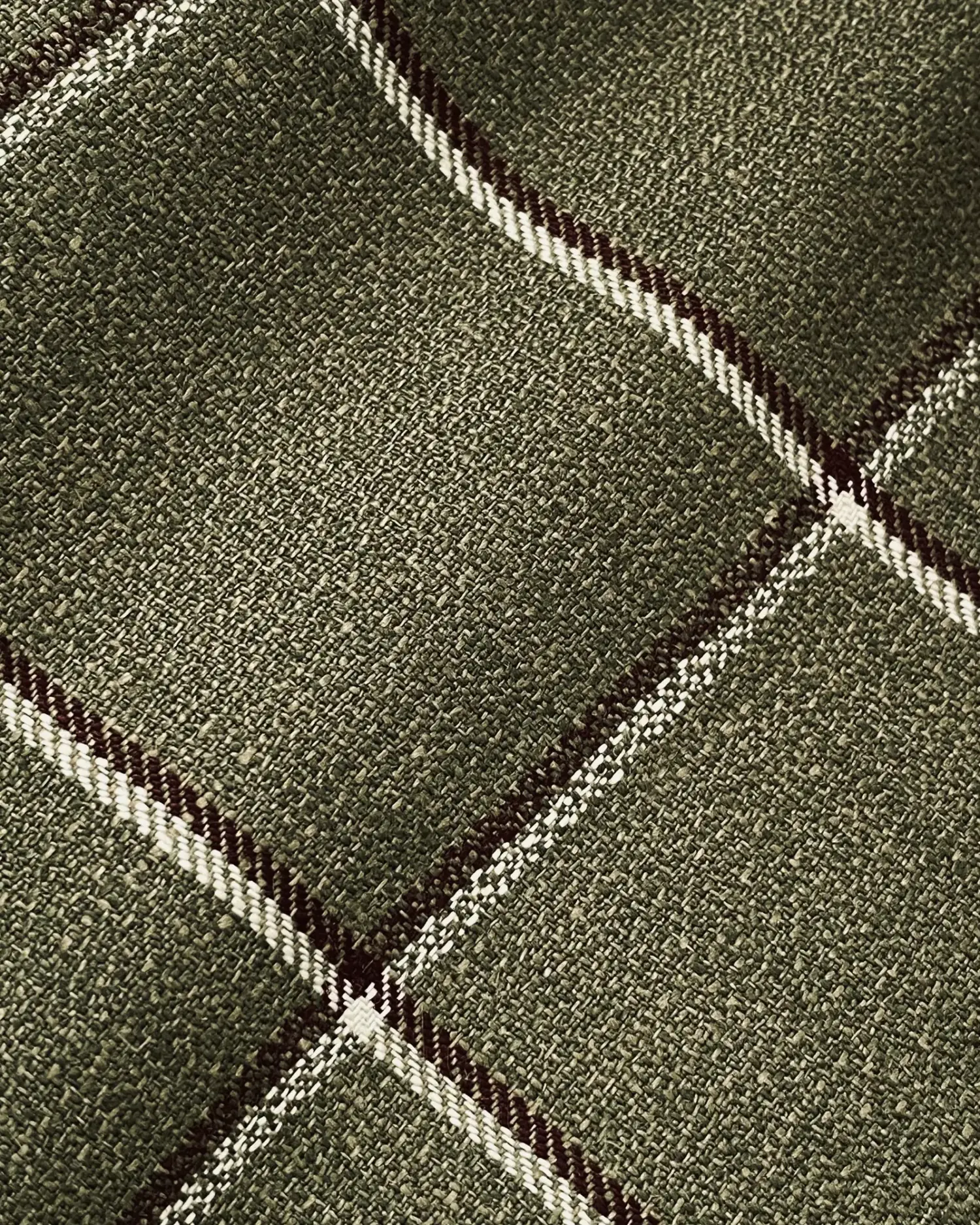Close-up of a green plaid fabric with white and dark stripes creating a crosshatch pattern.