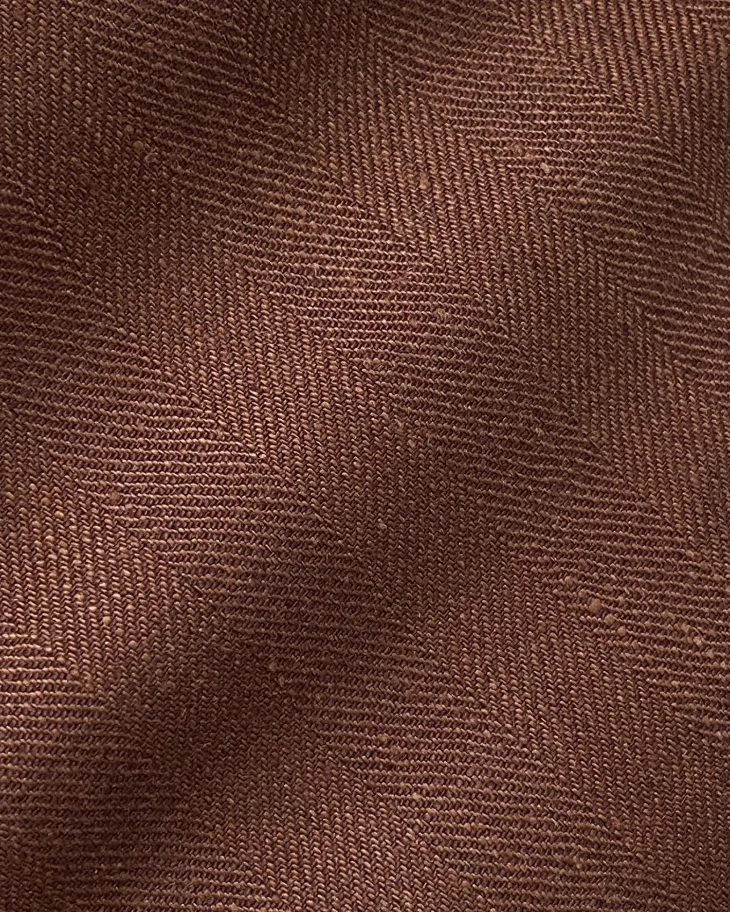 Close-up of brown herringbone fabric texture featuring diagonal patterns and rich color detail.